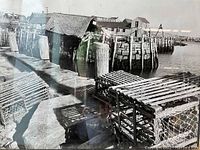 Close-up view of the black and white photograph showing lobster traps on a dock and waterfront buildings.