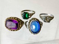 Photo showing four Victorian costume jewelry rings from a top and angled view, highlighting various colored stones and metal bands.