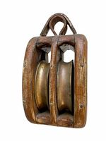 Side angled view of the antique double pulley showing two bronze wheels encased in a wooden frame with metal top attachment.
