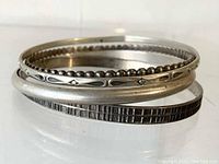 Stack of four sterling silver bangles showing different surface textures and designs.