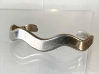 Front side of wavy sterling silver bangle showing smooth, reflective surface and wave-shaped design.