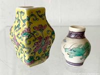 Two tiny Chinese hand painted vases showing front and side views, one yellow with floral design and one smaller with dragon design