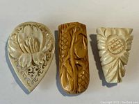 Front view showing detailed carving of three scarf clips with floral and fruit motifs