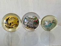 Front view of trio of vintage Chinese reverse painted glass orbs showing colorful detailed artwork on each orb, set on a flat surface with clear reflections.
