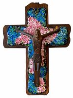 Front view of vintage enameled metal crucifix showing colorful enamel floral patterns and metal figure of Christ on wooden cross base.