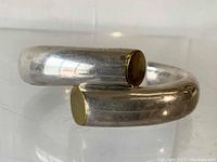 Close up side view of the bracelet showing its thick sculptural curved shape and brass/gold-tone capped ends