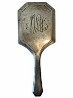 Front view of the vintage sterling silver hand mirror showing engraved monogram initials 'M H L' with patina and tarnish consistent with age.