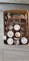 Top-down view of cardboard box filled with clear glass mason jars with various metal lids and screw bands organized neatly.