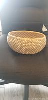 Beige woven round basket shown on a dark office chair with side view