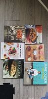 Photo showing seven assorted cookbooks laid out flat on wood floor. Titles visible include Biba's Italy, Jamie Oliver, Risotto, On Boards, and others.