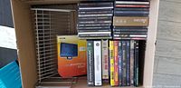 Photo of DVDs, CDs, PC DVDs, and game discs stacked in a metal rack with visible titles including Kill Bill volumes, Ghost in the Shell, and multiple Command & Conquer game discs and music CDs.