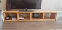 Front view of IKEA bookshelf under a TV, showing four open compartments and soft corner bumpers attached for baby proofing.