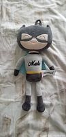 Front view of the plush toy showing details of the head, face, and front outfit with the word 'Maho'.