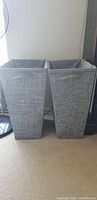 Front view of the two tall grey fabric laundry baskets placed side by side showing their textured exterior and open lids folded back.
