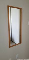 Photo of rectangular wall mirror hanging on wall showing wood frame and reflective glass surface