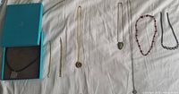 Wide shot of all jewelry items laid out on white fabric showing necklaces and bracelets alongside Hermes box.