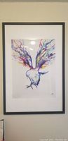 Photo of black picture frame with white mat and colorful bird painting inside. The frame is rectangular with thin edges.