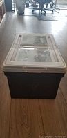 Front of plastic document filing box with lid on hardwood floor in office setting.