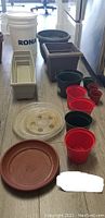 Photo showing a collection of varying sizes of plastic garden pots and trays arranged on the floor.