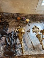 Photo of brass and cast iron wall mount candle holders alongside a three candle tabletop holder with colored candles on countertop.