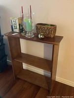 Wooden shelving unit with items on top including hurricane vase candle, decorative plant pot, and tall red candles.