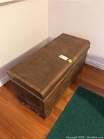 Full side and top view of the cedar chest showing the rectangular shape, slightly curved lid, worn wood, and some veneer damage.