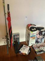Photo of Koolatron cooler in box, fishing rods, golf umbrella, golf driver cover, Wild Cat battery pack, and Monopoly game on floor against wall.