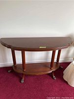 Full view of the solid wood demi lune table with curved top, lower shelf, and claw feet on carpeted floor