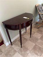 Front view of half-moon shaped solid wood demi lune table with mahogany finish on tiled floor.
