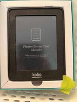 Front display of Kobo Mini eReader powered on with a charging prompt visible on the screen, inside the original box.