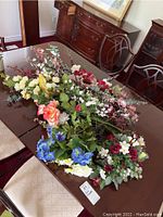 Wide view of assorted faux flowers on table showing various colors and types of flowers with greenery.