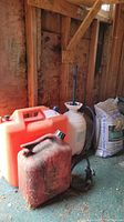 Photo showing both gas cans, the Flowmaster sprayer, and two bags of limestone screening placed on a green surface in a shed with wooden walls.