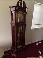 Full view of tall mahogany wood finish grandfather clock standing against wall.