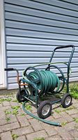 Garden hose reel on wheeled metal frame with green hose wrapped around. Corrosion visible on metal parts.