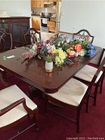 Full view of the dining table with artificial flowers, showing the intact rectangular top and surrounding chairs.
