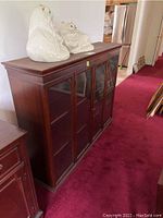 Full side-angle view of solid wood hutch with four glass panel doors and two white ceramic cat statues on top