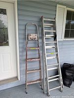Overall view showing both aluminum ladders side by side: one tall extendable ladder and one smaller painter's ladder with paint marks.
