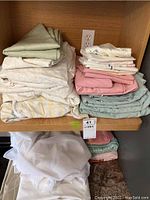 Folded sheets and linens stacked on a wooden shelf, including printed, pastel, and striped fabrics