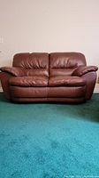 Front view of brown leather loveseat on green carpet.