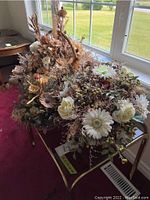 Overall view of gold plated metal side table with glass top and three faux flower baskets on top by a window