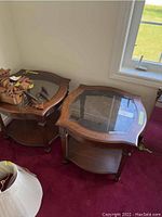Two solid wood side tables with glass tops and scalloped wooden frames placed on burgundy carpet near a window and wall.