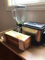 Photo showing the three kitchen appliances on a table: Potato Chipper box in front, blender with glass jug, and Toastess mini deep fryer.