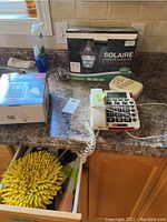 Kitchen countertop with two solar landscape light boxes, a white corded landline telephone with large buttons, and a First Alert carbon monoxide detector.