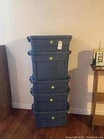 Stack of five grey plastic storage totes with lids, viewed from front against wall.