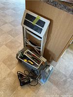 Photo showing a gray metal step ladder, gray plastic toolbox filled with hand tools like pliers and screwdrivers, yellow tape measure, and black Craftsman electric drill on the floor.