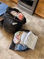 Two large black bags filled with various folded towels, linens, and curtains