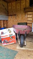 Homelite Mighty Lite backpack blower box next to a red metal wheelbarrow inside a wooden shed