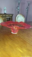 Red and clear wavy glass bowl displayed on wooden table with furniture in the background.
