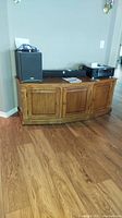 Wood entertainment cabinet against a wall on hardwood floor with electronic equipment on top.