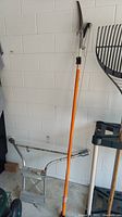 Full view of the Fiskars tree pruner standing upright showing single cutting head and orange pole.
